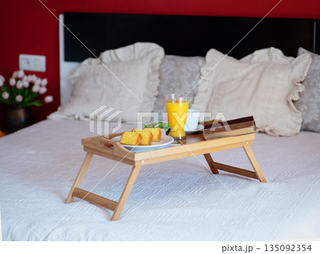 Breakfast served in bed on a wooden tray with tea, juice, cookies. Hotel room service, relax concept Breakfast served in bed on a wooden tray with tea, juice, cookies. Hotel room service, relax concept 135092354