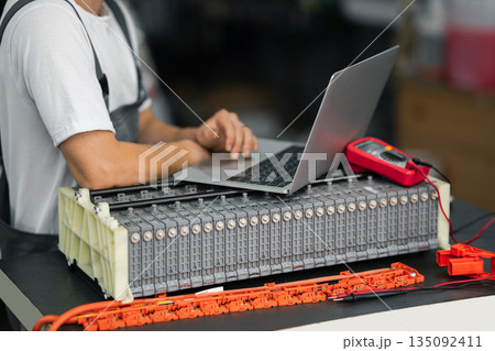 Serviceman repairs electric battery pack of hybrid car using laptop 135092411