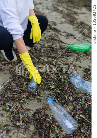 volunteer collecting plastic bottles on a polluted beach, highlighting ocean pollution, waste problem, environmental protection and coastal cleanup action. volunteer collecting plastic bottles on a polluted beach, highlighting ocean pollution, waste problem, environmental protection and coastal cleanup action. 135092425