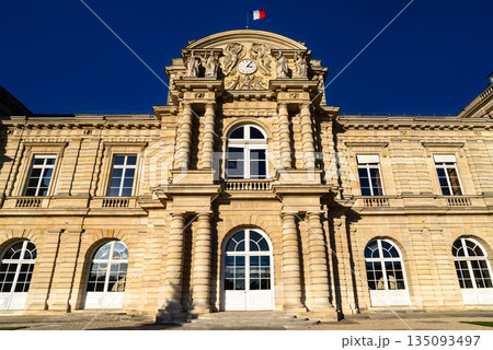 Luxembourg Palace stands in the Jardin du Luxembourg in Paris, France. Historic stone facade of the French Senate building features columns and a clock under a blue sky 135093497