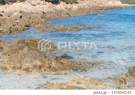 Rocky Mediterranean shoreline with clear blue water and natural stone textures. Sunny summer day, calm sea and untouched coastal landscape. Ideal for travel, nature and vacation concepts., La 135094141