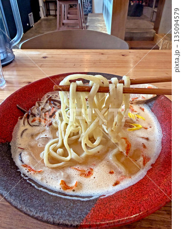 Close up of thick udon noodles being lifted from a creamy broth with chopsticks 135094579