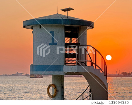 Lifeguard tower with spiral staircase at sunset over the ocean with boats 135094580