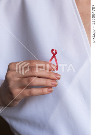 A doctor holds a red ribbon in their hand, symbolizing awareness for World Cancer Day on February 4th. The doctor wears a white coat and shows commitment to cancer awareness. 135094707