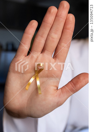 A doctor holds a gold ribbon in their palm, symbolizing support for childhood cancer awareness on International Childhood Cancer Day, February 15th. A doctor holds a gold ribbon in their palm, symbolizing support for childhood cancer awareness on International Childhood Cancer Day, February 15th. 135094713