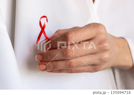 A doctor holds a red ribbon in their hand, symbolizing awareness for World Cancer Day on February 4th. The doctor wears a white coat and shows commitment to cancer awareness. 135094718