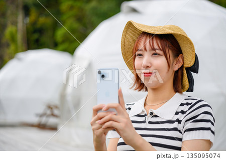 ドームテントでスマホ撮影を楽しむ女性 【撮影協力：隠岐シーサイドリゾートみやび様】 135095074