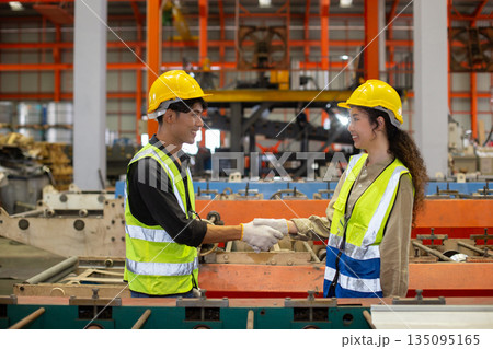 Two industrial worker wearing safety helmet and reflective vests shake hands inside manufacturing factory, symbolizing teamwork, trust collaboration successful industrial. accept approve agreement. Two industrial worker wearing safety helmet and reflective vests shake hands inside manufacturing factory, symbolizing teamwork, trust collaboration successful industrial. accept approve agreement. 135095165