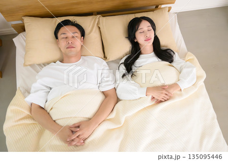 寝室のベッドで2人で並んで眠る男女 135095446