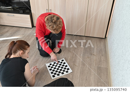 Two people playing chess on the floor in a home during daytime Two people playing chess on the floor in a home during daytime 135095740