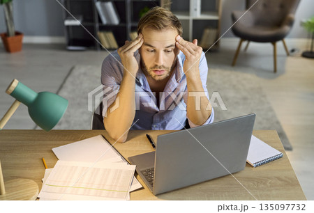 Stressed man at laptop amid papers facing accounting audit crisis at home office Stressed man at laptop amid papers facing accounting audit crisis at home office 135097732
