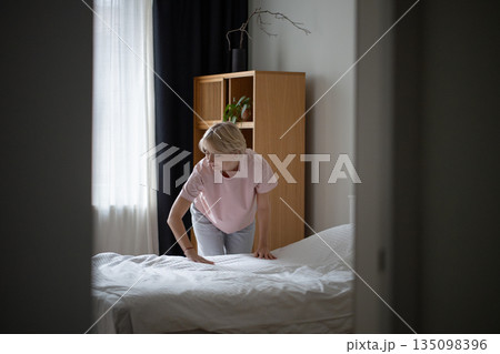Peaceful positive woman arranging bed in early morning after sleep, practicing self love routine. Peaceful positive woman arranging bed in early morning after sleep, practicing self love routine. 135098396