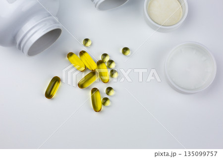 Fish oil capsules. Dietary supplements are scattered across white table, isolated. Set of vitamins for dietary supplements. White table with vitamin capsules and jars Fish oil capsules. Dietary supplements are scattered across white table, isolated. Set of vitamins for dietary supplements. White table with vitamin capsules and jars 135099757