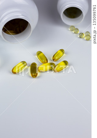 Vertical photo of Omega 3 and vitamin D3 capsules with K2 on white background near jars. Dietary supplements for improving wellbeing. Capsules with set of vitamins for improving health Vertical photo of Omega 3 and vitamin D3 capsules with K2 on white background near jars. Dietary supplements for improving wellbeing. Capsules with set of vitamins for improving health 135099761