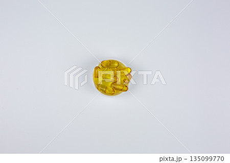 Vitamin D, omega 3, omega 6. Food supplement oil filled fish oil, flaxseed oil. Yellow dietary supplement capsules in lid on white background. Omega 3 capsules are in center of frame Vitamin D, omega 3, omega 6. Food supplement oil filled fish oil, flaxseed oil. Yellow dietary supplement capsules in lid on white background. Omega 3 capsules are in center of frame 135099770