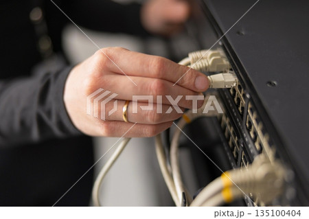 Adult IT technician setting up network cables in a data center and performing maintenance Adult IT technician setting up network cables in a data center and performing maintenance 135100404