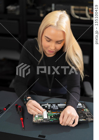 Woman IT technician works on laptop hardware during repair and upgrade in a workshop 135100419