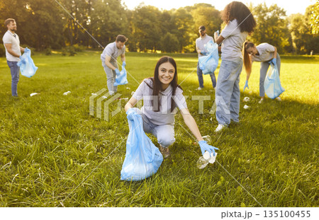 Diverse group of people, friends volunteering in sunny, grassy green park, picking up litter Diverse group of people, friends volunteering in sunny, grassy green park, picking up litter 135100455