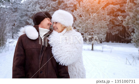 Models Exchanging Gentle Caresses Amidst Winter Forest, Tender Couple Embraces Under Snowy Pine Trees With Warm Lighting, Elegant Models In Furlined Attire Share Loving Kiss In Frosty Forest Glow 135100731