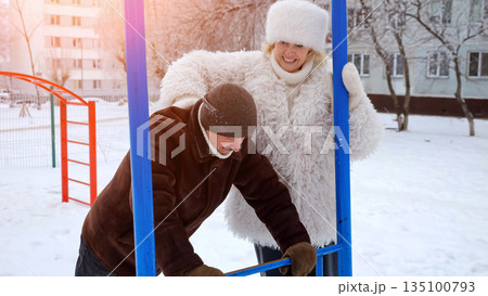 Couple Exercises Outside, Outdoor Workout Session In Snowy Courtyard With Couple Of Campions, Pair Of Individuals Practicing Strength Exercises At Outdoor Gym Amidst Snowcovered Courtyard 135100793