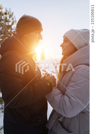 Couple Holding Hands At Sunset, Warm Backlight Creating Silhouette Effect As Partners Exchange Meaningful Gaze And Gentle Touch, Winter Coats And Knit Hats Framing Candid Romantic Moment, Soft Golden 135100811