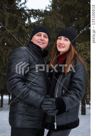 Pair Dressed Warmly Beside Evergreen Background, Two Individuals Wearing Coats And Hats In Urban Setting, Couple Exuding Fashion In Winter Attire With City Vibe And Cozy Atmosphere Pair Dressed Warmly Beside Evergreen Background, Two Individuals Wearing Coats And Hats In Urban Setting, Couple Exuding Fashion In Winter Attire With City Vibe And Cozy Atmosphere 135100818