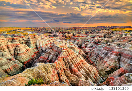 Big Badlands Overlook stands in Badlands National Park, South Dakota, USA. Scenic view features colorful eroded rock formations and sedimentary layers under a cloudy sunset sky Big Badlands Overlook stands in Badlands National Park, South Dakota, USA. Scenic view features colorful eroded rock formations and sedimentary layers under a cloudy sunset sky 135101399