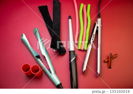 A pleat on a pink background, stylers and curling irons for straightening and creating curls, curlers of different shapes and sizes nearby. The concept of hair care, hairstyle, hairdressing. High A pleat on a pink background, stylers and curling irons for straightening and creating curls, curlers of different shapes and sizes nearby. The concept of hair care, hairstyle, hairdressing. High 135102019