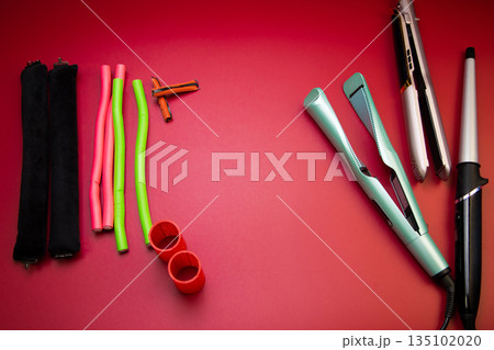 On the side there are stylers and curling irons for straightening and creating curls, on the other side there are curlers of different shapes and sizes on a pink background with space for text. The 135102020