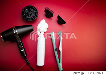 Top view of hair styling foam in a white bottle, surrounded by a hairdryer and hair dryer attachments and a curling iron on a pink background with space for text. The concept of long-term hair styling 135102021