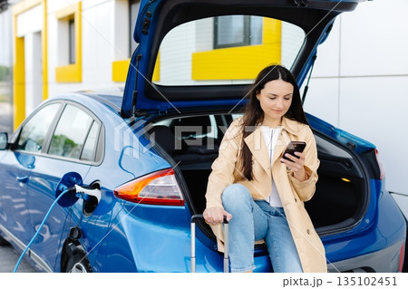 Young woman waiting charging automobile battery from small public station and using smartphone while charging automobile Young woman waiting charging automobile battery from small public station and using smartphone while charging automobile 135102451
