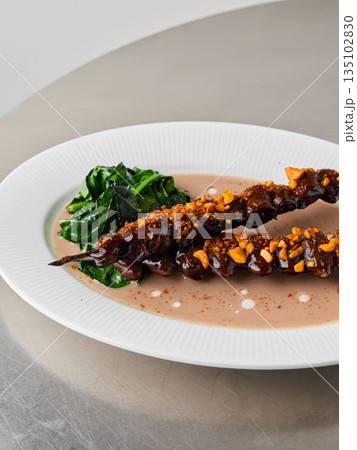 Photograph emphasizing glazed meat skewer and wilted vegetable garnishes Photograph emphasizing glazed meat skewer and wilted vegetable garnishes 135102830