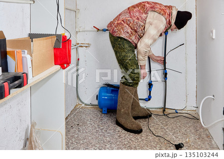Homeowner secures heating cable to incoming house pipe with plastic ties in unheated utility room of rural house. Homeowner secures heating cable to incoming house pipe with plastic ties in unheated utility room of rural house. 135103244