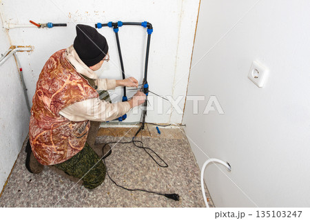 After disconnecting country house from water supply man installs heating cable on incoming pipe to prevent rupture during winter frosts. After disconnecting country house from water supply man installs heating cable on incoming pipe to prevent rupture during winter frosts. 135103247
