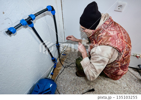 While preparing country house for winter frosts homeowner installs heating cable on incoming pipe. 135103255
