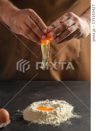 Breaking fresh egg into flour on dark table, close up cooking process Breaking fresh egg into flour on dark table, close up cooking process 135103427