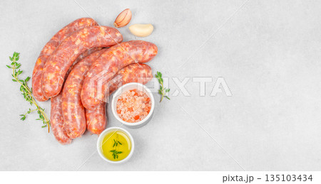 Raw sausages with olive oil, garlic, thyme and salt on light stone background with copy space, top view 135103434