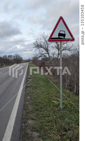 Slippery road sign signals potential danger in cloudy weather 135103458
