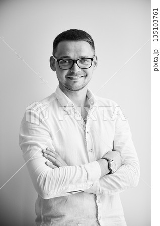 Charming man smiling straight to camera. Portrait of handsome young male in casual clothes keeping arms crossed while standing on white background. Black and white image. 135103761