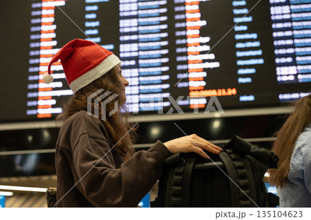 Woman wearing Santa hat checking flight schedule at airport during Christmas holidays Woman wearing Santa hat checking flight schedule at airport during Christmas holidays 135104623