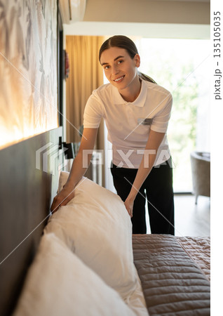 Young woman in hotel uniform doing bed in a hotel room 135105035