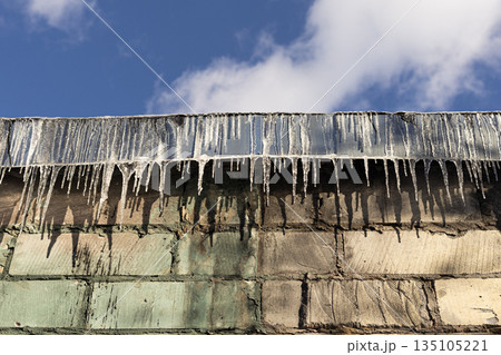 Icicles hanging from the roof edge of a residential house in winter weather Icicles hanging from the roof edge of a residential house in winter weather 135105221