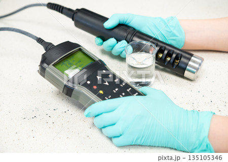 Female hands in protective gloves measuring water pH with a field pH meter. Female hands in protective gloves measuring water pH with a field pH meter. 135105346