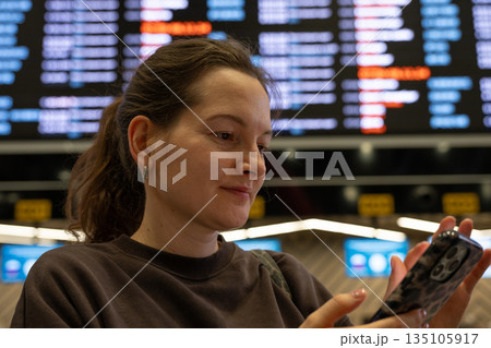 Woman using smartphone and checking flight schedule at airport 135105917