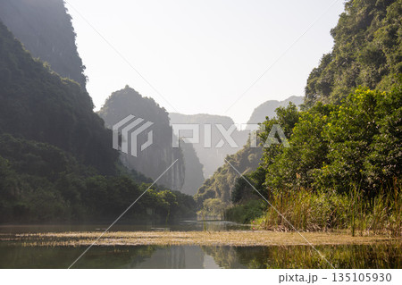 Landscape of Ninh Binh reflecting on the river at sunrise with hazy mountains Landscape of Ninh Binh reflecting on the river at sunrise with hazy mountains 135105930