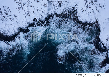 Aerial View of Waves Crashing on Snowy Coastline 135105936