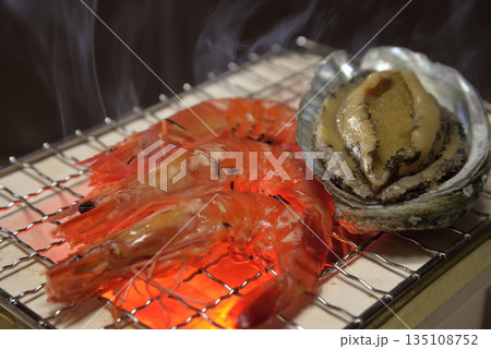 煙り立ち昇る七輪でアワビと海老を焼く 135108752
