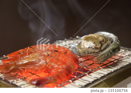 煙り立ち昇る七輪でアワビと海老を焼く 135108756