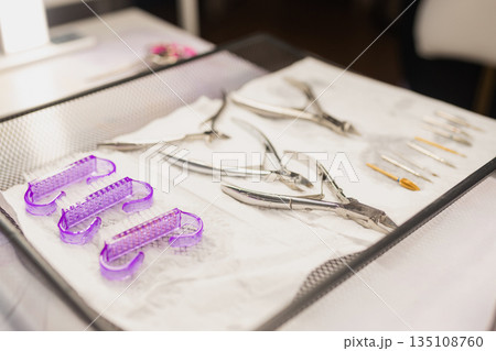 Professional manicure tools set prepared for nail care procedure. Scissors, cuticle nippers and drill bits arranged on sterile surface in beauty salon. Nail service and hygiene concept. Professional manicure tools set prepared for nail care procedure. Scissors, cuticle nippers and drill bits arranged on sterile surface in beauty salon. Nail service and hygiene concept. 135108760