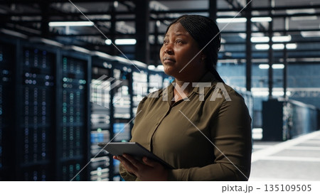 Data center software developer uses tablet to develop disaster recovery plans, minimizing downtime. IT worker in server hub enhancing data protection protocols using device, camera B close up Data center software developer uses tablet to develop disaster recovery plans, minimizing downtime. IT worker in server hub enhancing data protection protocols using device, camera B close up 135109505